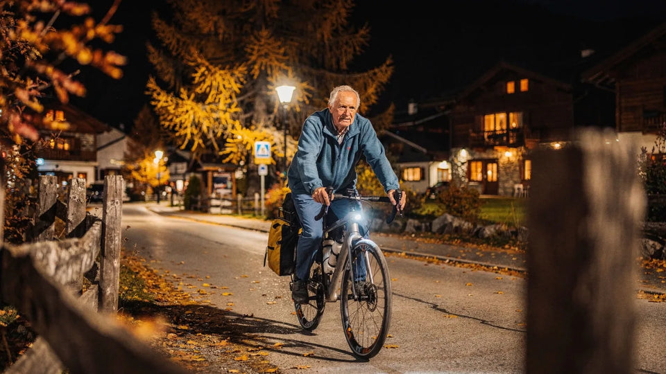 älterer Radfahrer in einer Bergstadt, im Herbst, abends im Licht von Fahrradlicht und Laternen