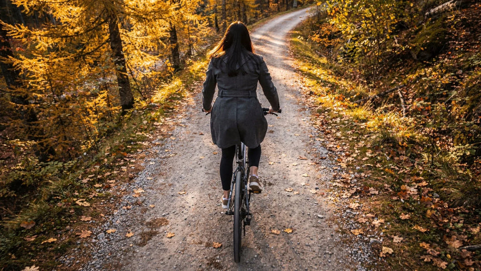 Radfahrerin um die 40 auf einem Waldweg, im Herbst, bei hellen Wolken und durchbrechender Sonne