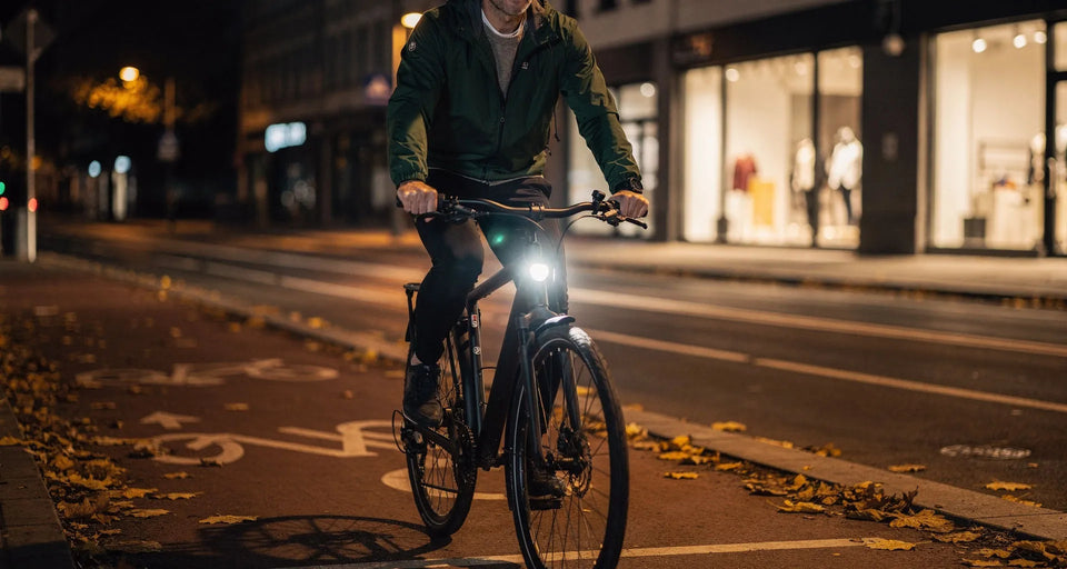 Radfahrer in grüner Jacke abends auf einem Stadtradweg mit eingeschaltetem Licht