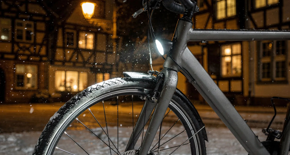 Vorderrad mit leuchtendem Fahrradlicht bei Schneefall in einer Altstadt am Abend
