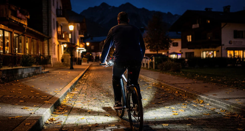 Radfahrer am Abend auf Kopfsteinpflaster in einem Bergort, Laternen und Fahrradlicht