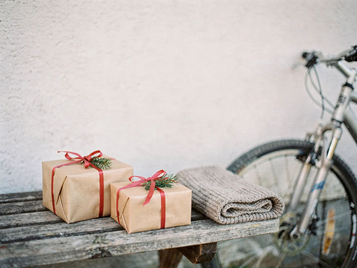 Geschenke für Radfahrer – verpackte Päckchen und Schal auf einer Holzbank, dahinter ein Fahrrad
